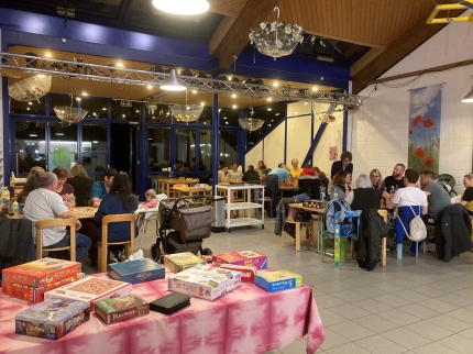 Tisch mit Gesellschaftsspielen im Vordergrund, dahinter Sechsertische mit spielenden Leuten.