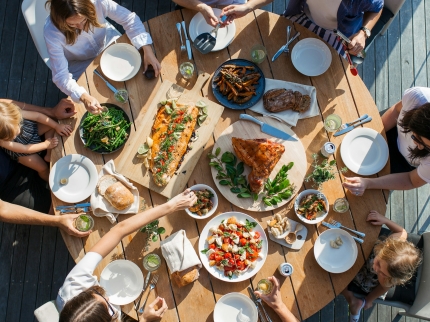 Erwachsene und Kinder sitzen um einen Tisch und essen zusammen.