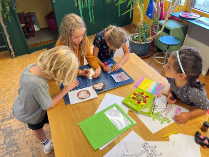 Kinder gestalten eine Druckvorlage und zeichnen am Tisch.