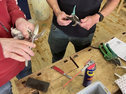 Zwei Personen reparieren Gartenscheren an einem Werkbank.