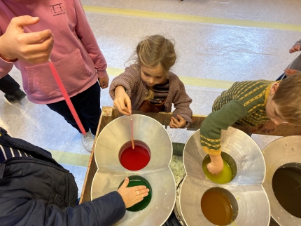 Kinder und Erwachsene stehen um die Wachsgefässe und ziehen bunte Kerzen.