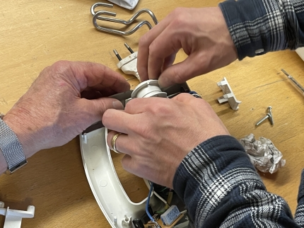 Drei Hände arbeiten am Innenleben eines Handmixers.