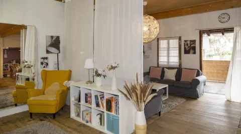 Vorne gelber Lesesessel mit niedrigem Bücherregal und dahinter gemütliche Sofas mit Tisch